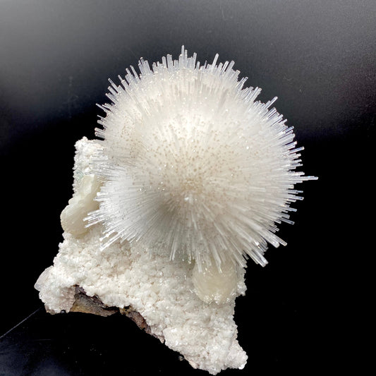 Glassy white mesolite needles in a spherical formation formed with stilbite and apophyllite on a mordenite matrix. Calcite adds smoky coloration to the end of each needle.